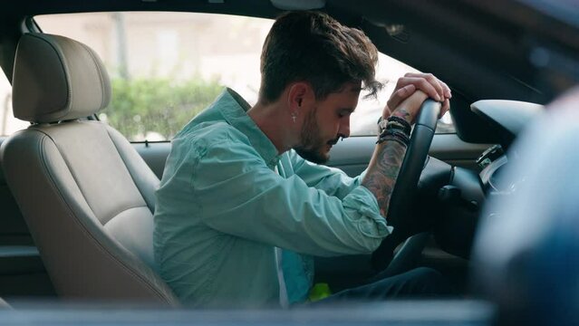 Young hispanic man stressed driving car at street