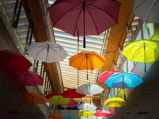 Fototapeta na wymiar Colourful umbrellas as decoration in a shopping mall. Looking to the ceiling in the building. Opened umbrellas are flying around. Pattern of brollies inside in a shopping center.
