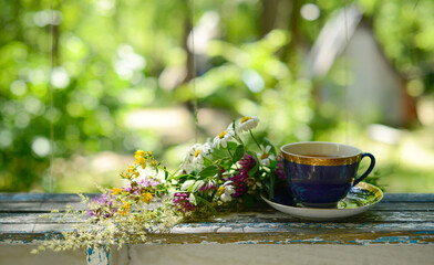 Obraz na płótnie Canvas Cup of herbal tea and bouquet chamomile flowers and wildflowers on wooden table in garden, blurred background, soft focus