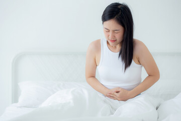 Young asian woman sitting on bed pain stomach or bowel with disease constipation in the bedroom at home, unhappy female sick and menstruation and stomachache, medical and health concept.