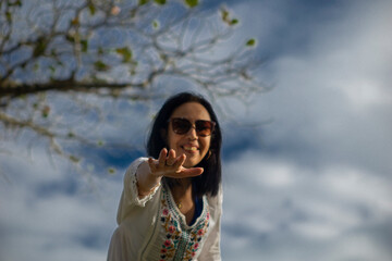 elderly woman enjoying trip, tree and blue sky in the background reaching out her hand and smile