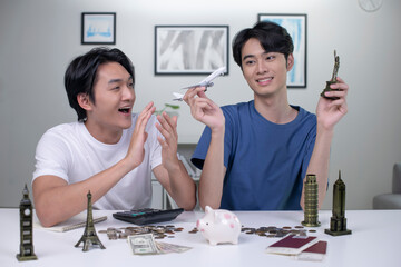 Young Asian gay couple plans to save money for a trip around the world. Travel budget concept. passport, monument model and aircraft toy in the picture. Lgbt couple lifestyle.