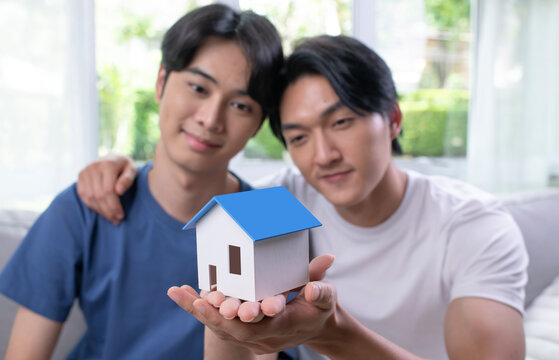 Young Asian gay couple is holding a model house in hand, LGBT male couple saving money for family and home, new home.