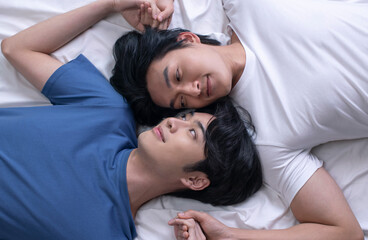 High angle view of smiling Asian gay couple relaxing and lying down in bed. LGBT male couple lifestyle concept.