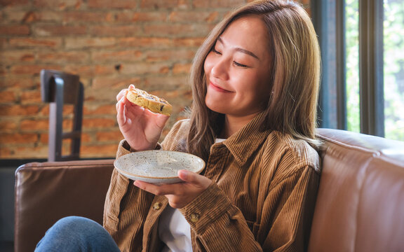 Portrait image of a beautiful young asian woman holding and eating a piece of cookie