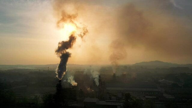 Air pollution from industrial chimneys and enterprise chimneys tubing against the sky-sunset background release black smoke. Factory pollutes environment