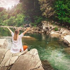 Woman doing yoga on the stone at the mountain river. Carpathians