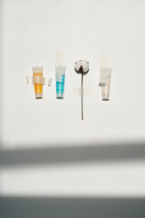 Cosmetics of different colors and a sprig of cotton on a white background with tape.