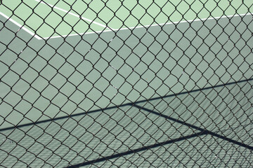 Fototapeta premium Abstract view of all weather green tennis court, looking through diamond wire fencing