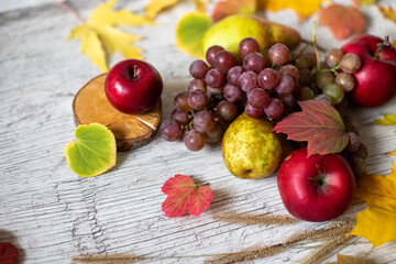 Still life with leaves and fruits. Autumn still life. Delicious fruits on a wooden table with autumn yellow leaves. Apples, grapes, pears. Bright colors of autumn