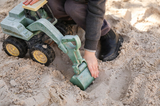 Preschool child playing in sandbox with green digger at kindergarten