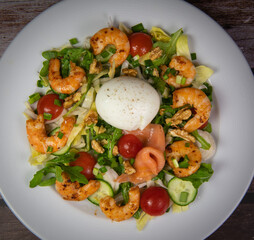 Recipe for rocket salad, endive, tomato, cucumber, soft-boiled egg, fried shrimp with paprika, smoked salmon and nuts. High quality photo
