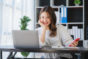 Beautiful Asian businesswoman working on a desk with a laptop with a smiling face while looking at the document received in the office.