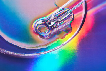 Pipette with sample of cosmetic product in petri dish on holographic background, iridescent...