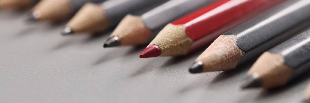 Pencils tips put on grey surface in strict order, red one among black pens
