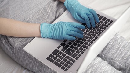 Young business woman wears medical face mask gloves working on laptop computer sitting at home office desk.