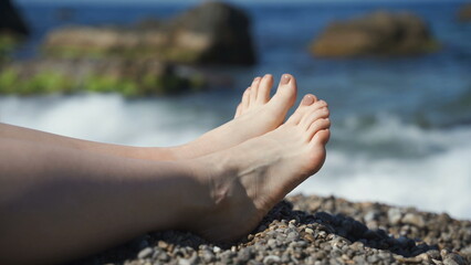 Female legs on the background of the beach on the sea of pebbles. Rest and relaxation, slow motion, vacation