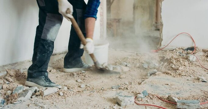 Busy builder collecting construction debris with a shovel. Home renovation demolition of walls.