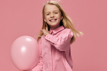 joyful, friendly little girl stands and plays with a pink balloon on a pink background in a pink shirt. The theme of delight and happiness