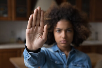 Serious African teenager girl looking at camera raises her palm showing stop gesture, against...