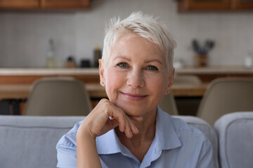 Baby boomer female head shot portrait. Attractive middle-aged woman sits on couch, relaxing alone...