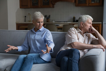 Wound up older wife expresses her displeasure to annoyed husband sit together on sofa at home. Aged...