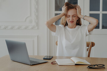 Exhausted woman holds her head. Freelancer has deadline and working from home in evening.