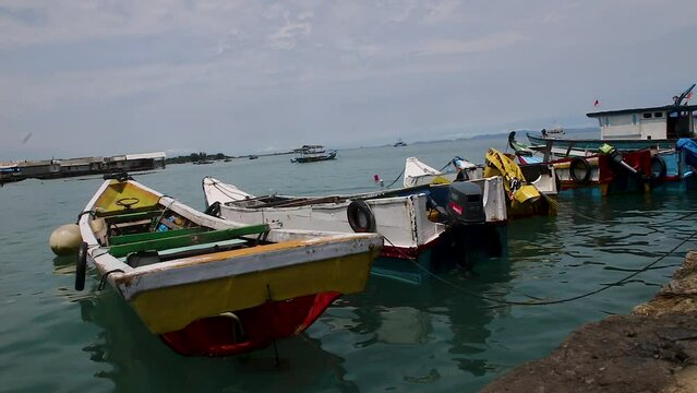 The view during the day, several traditional fishing boats leaning on the beach. against a backdrop of the open sea.