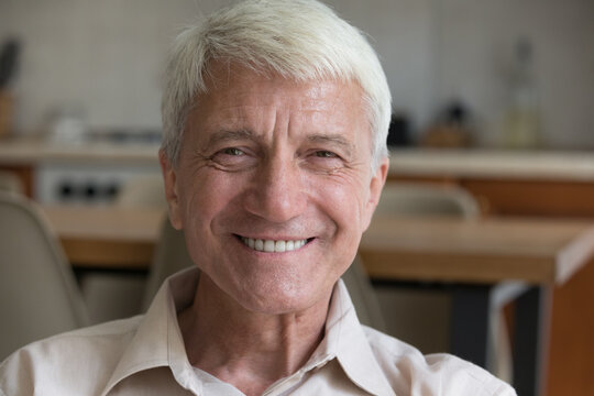 Head Shot Close Up Mature 60s Man Sits On Sofa Look At Camera, Having Wide Toothy Smile Feel Happy Enjoy Carefree Retired Life Relax Indoor. Medical Insurance For Older, Baby Boomer Person Portrait