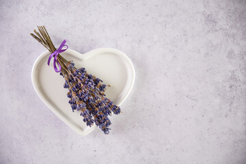 Dried lavender branches in a white porcelain heart on a light gray background with copy space. Decoration for Valentine's Day, birthday, Mother's Day, wedding.