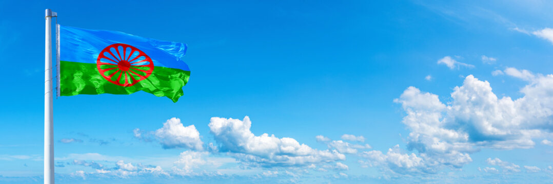 Romani people flag waving on a blue sky in beautiful clouds - Horizontal banner