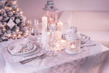 Festive  Christmas table place setting with silverware, candles and decorated Christmas tree