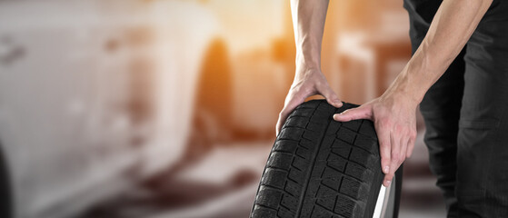Car tire shop and service. Mechanic holding winter tyre on garage background. Copy space