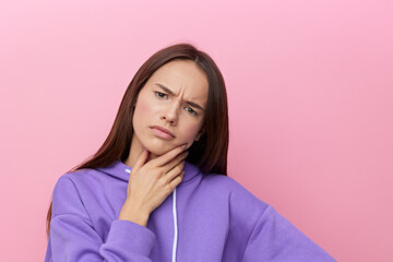 a sullen woman stands full-face on a pink background in a purple suit looks forward with dislike touching her chin with her hand