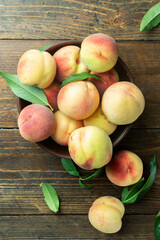 Fresh sweet peaches on the wooden table, selective focus. Fresh ripe peaches with leaves in a bowl on a wooden background.
