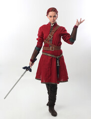 full length portrait of beautiful woman wearing a red medieval fantasy warrior costume with leather armour, holding weapons.  Standing pose isolated on white studio background. © faestock