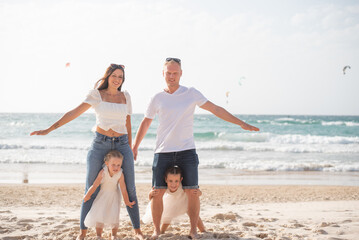 Happy family: parents and two daughters walking on beach in summer vacation. Run, play and get fun on sand near sea together. white clothes and jeans. 