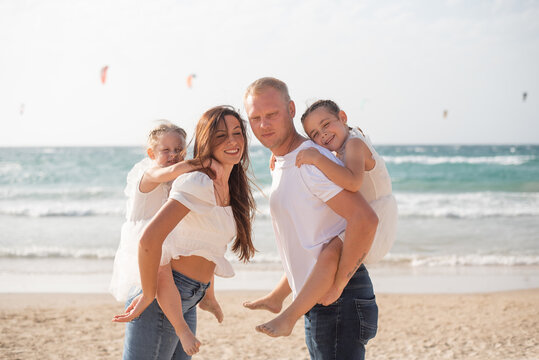 Happy family: parents and two daughters enjoy on beach in summer vacation. Run, play and get fun on sand near sea together. White clothes and jeans.