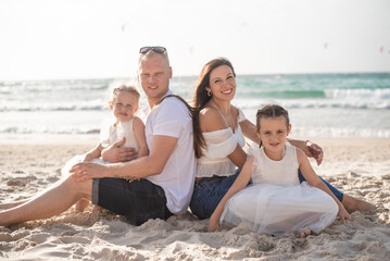 Summer vacation, happy family of four having fun. parents and two daughters sit on beach sea in summer day. white clothes and jeans. 