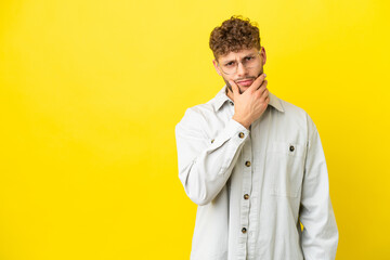 Young handsome caucasian man isolated on yellow background having doubts