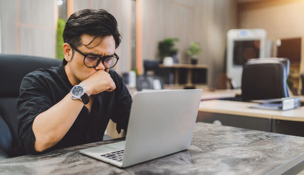 Asian business man stressed sitting headache. exhausted male employee have migraine while busy working at office. a looking tired guy work late overwork touch face because pain from office syndrome