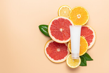 Сosmetic tube lying on composition of neatly arranged ripe grapefruit, orange, lemon, green leaves on beige background. Organic cosmetics with vitamin C Mockup