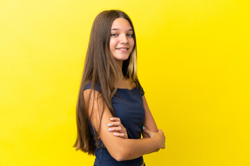 Little caucasian girl isolated on yellow background with arms crossed and looking forward