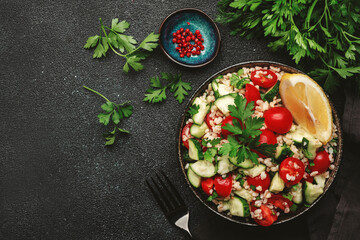 Bulgur tabbouleh salad with fresh tomatoes, cucumbers, parsley and lemon dressing. Traditional Middle Eastern and Arabic dish. Black stone kitchen table background, top view