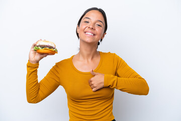 Young hispanic woman holding a burger isolated on white background giving a thumbs up gesture