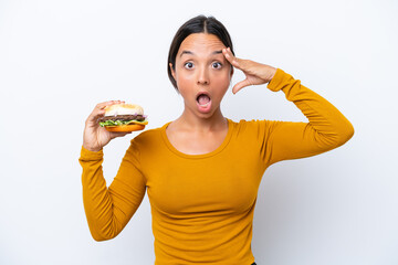 Young hispanic woman holding a burger isolated on white background with surprise expression
