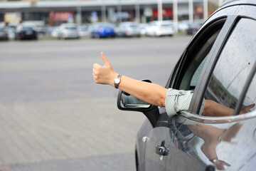 Dłoń kobiety, ręka wysunięta przez okno samochodu osobowego, suwa, na placu przed marketem.