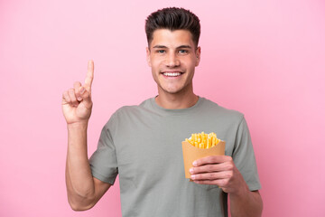 Young caucasian man holding fried chips isolated on pink background pointing up a great idea