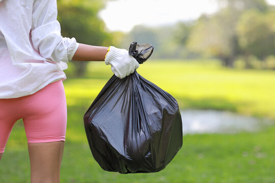 Rear View Young Beautiful Asian Volunteer Woman Hands Hold Garbage Bag And Picking Up Litter While Cleaning Plastic Bottle From Lawn During A Volunteering Environmental Cleanup Area Park Event Outdoor