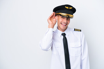 Airplane caucasian pilot isolated on white background listening to something by putting hand on the ear